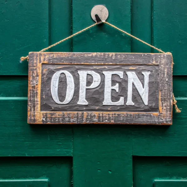 A vintage wooden open sign hanging on a rustic green door, symbolizing welcoming and accessibility.