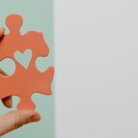 pexels-photo-8386182-8386182 Close-up of a hand holding a heart-shaped puzzle piece against a colorful background.